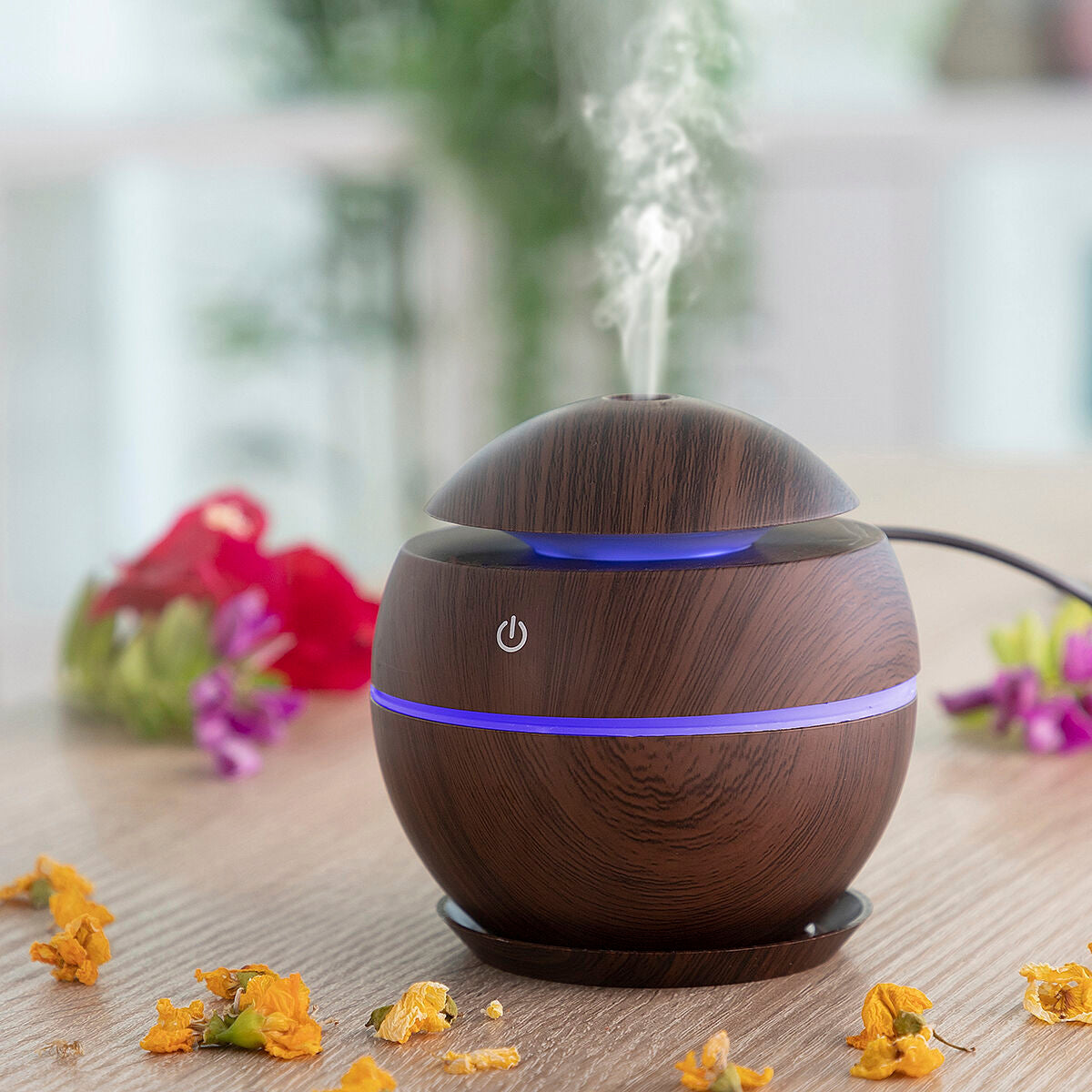 Wooden essential oil diffuser with blue light on a wooden surface with flowers in the background