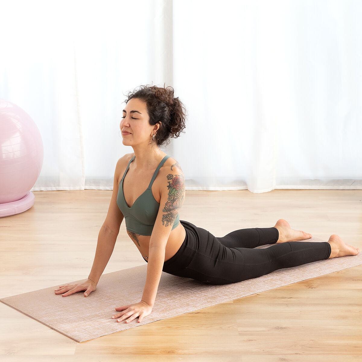 Woman practicing yoga on a mat in a bright room with large windows.