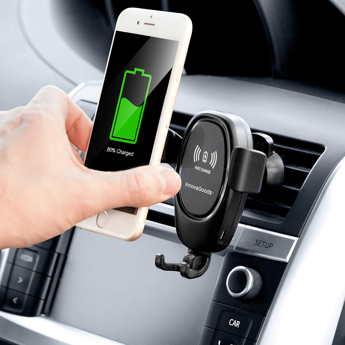 Hand holding a phone above a wireless car charger in a car's air vent.